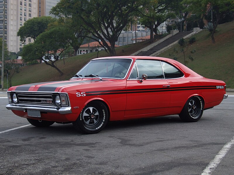 O **Opala SS** foi uma das versões mais esportivas e icônicas do **Opala**, produzido pela **Chevrolet** no Brasil entre os anos de 1968 e 1982. O modelo se tornou um símbolo de potência e estilo, especialmente nas versões mais avançadas, sendo considerado um dos carros clássicos da indústria automotiva brasileira. ### **Design Externo** - **Carroceria**: O Opala SS possuía a famosa carroceria do Opala, com linhas elegantes, mas de perfil mais robusto e musculoso, especialmente nas versões mais potentes. Seu design era uma mistura de sofisticação e agressividade, com proporções equilibradas e um aspecto "musculoso", típico dos sedãs esportivos da época. - **Frente**: A frente do Opala SS destacava-se pelos **faróis duplos** (em versões posteriores), que conferiam ao carro uma aparência mais imponente e esportiva. A grade dianteira era cromada, com um formato mais largo e reto, em estilo típico dos carros da década de 1970. O capô era mais pronunciado e, em algumas versões, contava com elementos de ventilação, proporcionando um visual mais agressivo. - **Rodas**: O Opala SS contava com rodas de aro largo, que conferiam ao carro uma postura mais agressiva e imponente. As rodas geralmente vinham com **aro cromado** ou com detalhes em **pintura preta** e tinham pneus de perfil mais baixo, em contraste com as versões mais simples do Opala. - **Traseira**: A traseira do Opala SS era mais compacta, com lanternas horizontais de tamanho médio e um acabamento limpo, sem exageros. Em alguns modelos, o **emblema "SS"** era um destaque, reforçando a identidade esportiva do modelo. - **Cores**: O Opala SS era oferecido em várias cores vibrantes, incluindo **vermelho**, **branco**, **preto**, e **azul**, que eram escolhidas para dar ao modelo um visual mais esportivo e arrojado. ### **Interior** - **Painel de instrumentos**: O painel do Opala SS era mais sofisticado que o das versões comuns do Opala. Ele contava com **mostradores analógicos** para velocímetro, tacômetro (contagem de giros do motor), medidor de combustível e temperatura, além de detalhes cromados. O design do painel tinha um toque de modernidade para a época, mas com um visual mais esportivo e direto. - **Banco e estofado**: O interior do Opala SS se destacava pelos bancos esportivos, mais envolventes e confortáveis, com acabamentos em **vinil** ou **tecido de alta qualidade**. Os bancos da frente eram muitas vezes individuais, reforçando a ideia de um carro de desempenho. O volante era de formato mais simples, porém com detalhes esportivos, e o painel de portas possuía acabamentos cromados e de bom gosto. - **Espaço**: O Opala SS era um carro de **cinco lugares**, com amplo espaço interno tanto para passageiros quanto para bagagens. Embora fosse um sedã esportivo, o Opala SS também oferecia conforto, com um bom nível de acabamento e ergonomia. ### **Motorização e Performance** - **Motorização**: O Opala SS ficou famoso por suas versões potentes, com motores **seis cilindros em linha** de até **4,1 litros**, oferecendo uma excelente performance. O motor **6 cilindros** de 4,1L era capaz de entregar até 155 cv (em versões mais potentes), o que proporcionava uma aceleração forte e um desempenho de velocidade impressionante para um sedã. - **Versões de motor**: Além do motor de 4,1L, o Opala SS também estava disponível com motores menores, como o **4 cilindros de 1,8L e 2,5L**, mas as versões **V6** eram as mais procuradas pelos fãs de desempenho. - **Transmissão**: O modelo foi equipado com **transmissão manual de 4 marchas**, com a opção de câmbio automático em algumas versões. A relação de marchas era bem ajustada para permitir uma condução esportiva e dinâmica. - **Performance**: O Opala SS entregava uma aceleração e velocidade de tirar o fôlego para a época, sendo comparado aos muscle cars americanos em termos de desempenho. A suspensão era independente nas rodas dianteiras, com eixo rígido na parte traseira, e o sistema de freios era mais robusto nas versões SS, com discos nas rodas dianteiras, permitindo uma melhor frenagem. ### **Características Técnicas** - **Suspensão**: A suspensão do Opala SS era projetada para oferecer mais estabilidade e desempenho, com suspensão independente nas rodas dianteiras e eixo rígido na traseira. Isso garantiu ao carro um bom equilíbrio entre conforto e desempenho nas estradas e no uso cotidiano. - **Freios**: Como mencionado, o Opala SS contava com freios a disco nas rodas dianteiras e tambor nas traseiras, um sistema eficiente para a época. ### **Legado** O **Opala SS** se tornou um ícone entre os carros esportivos brasileiros e permanece até hoje como um dos modelos mais desejados por colecionadores e entusiastas. Sua combinação de potência, estilo e conforto fez dele um símbolo da época, sendo altamente valorizado no mercado de carros antigos e clássicos. A versão **SS**, com seu desempenho superior e visual agressivo, trouxe um novo nível de esportividade ao Opala, garantindo um lugar de destaque na história dos carros brasileiros e consolidando o modelo como um dos grandes clássicos do Brasil.